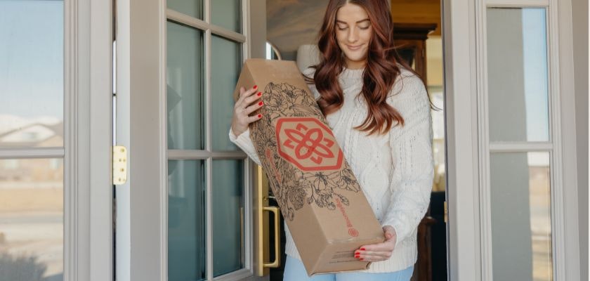 A woman receiving a beautifully packaged floral arrangement at her doorstep, smiling happily.