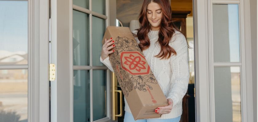 A woman in a cozy sweater receives a beautifully packaged flower delivery at home.