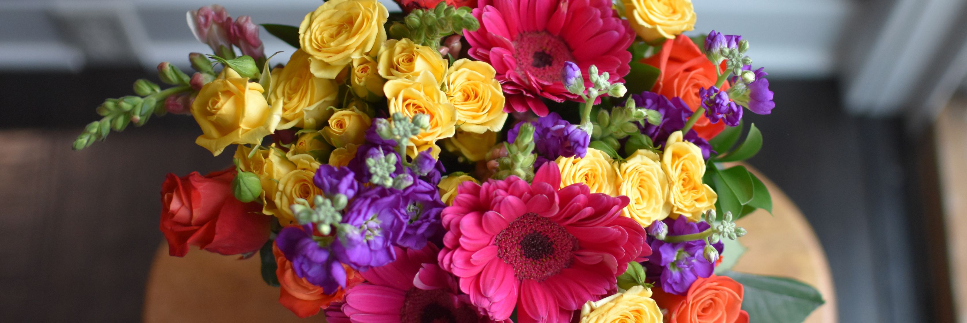 Vibrant floral bouquet featuring roses, gerbera daisies, and colorful blooms on a table.