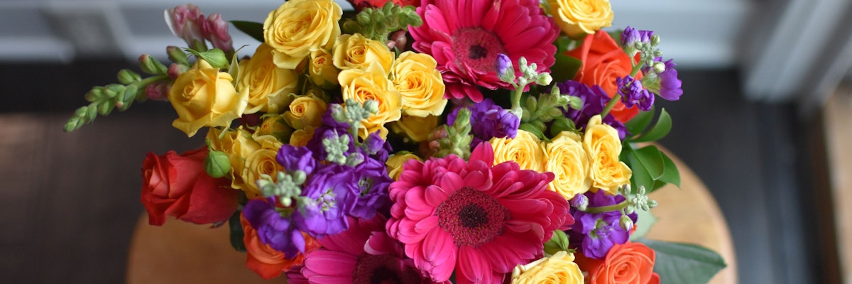 Vibrant floral bouquet featuring roses, gerbera daisies, and colorful blooms on a table.