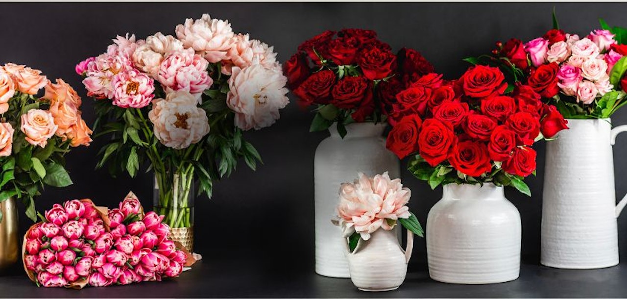 Vibrant floral display featuring red roses, peonies, and pink blooms in elegant vases.