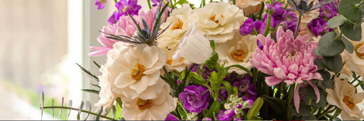 Elegant floral arrangement featuring creamy blossoms, purple asters, and lush greenery.