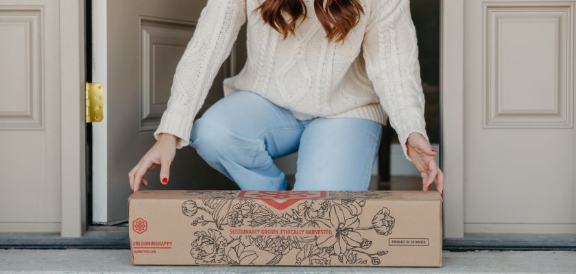 A woman in a cozy sweater receives a beautifully packaged floral delivery at her door.