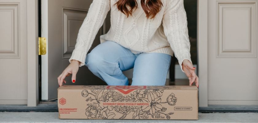 A woman in a cozy sweater receives a beautifully packaged floral delivery at her door.