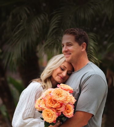 A couple sharing a tender moment, holding a vibrant bouquet of peach roses.