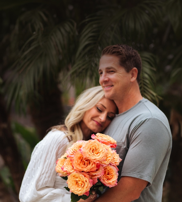 A couple sharing a tender moment, holding a vibrant bouquet of peach roses.