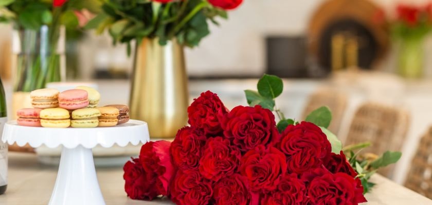 An elegant display of red roses in a vase with colorful macarons on a cake stand.
