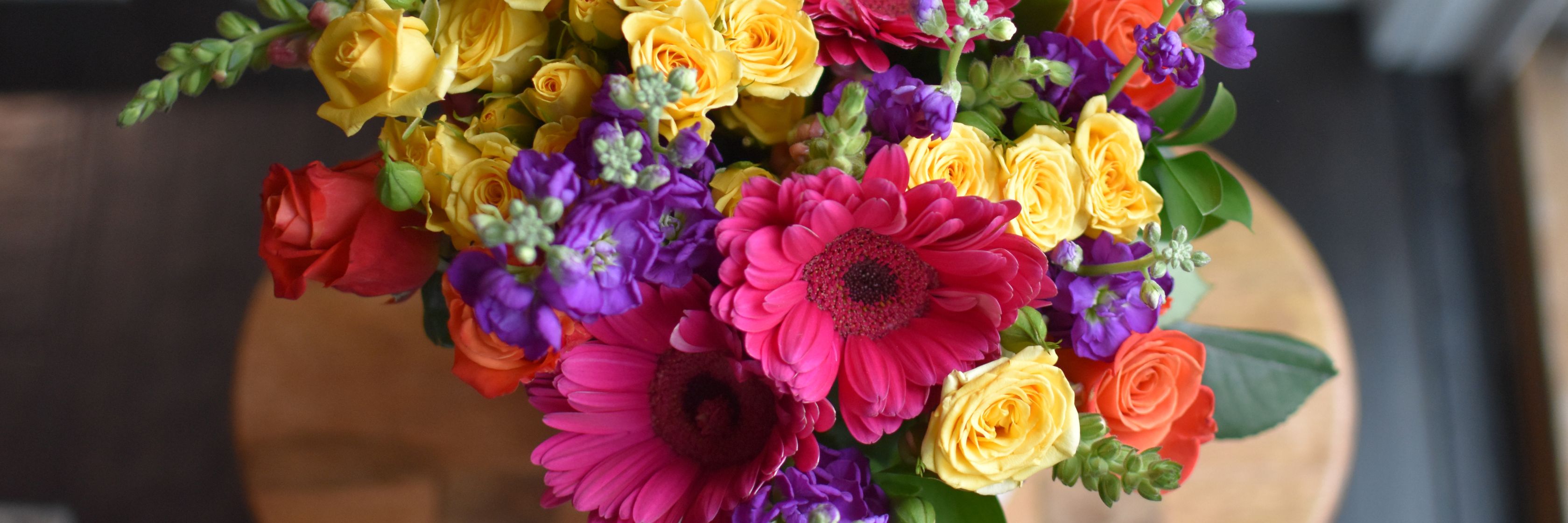 Vibrant floral arrangement featuring roses, gerbera daisies, and assorted colorful blooms.