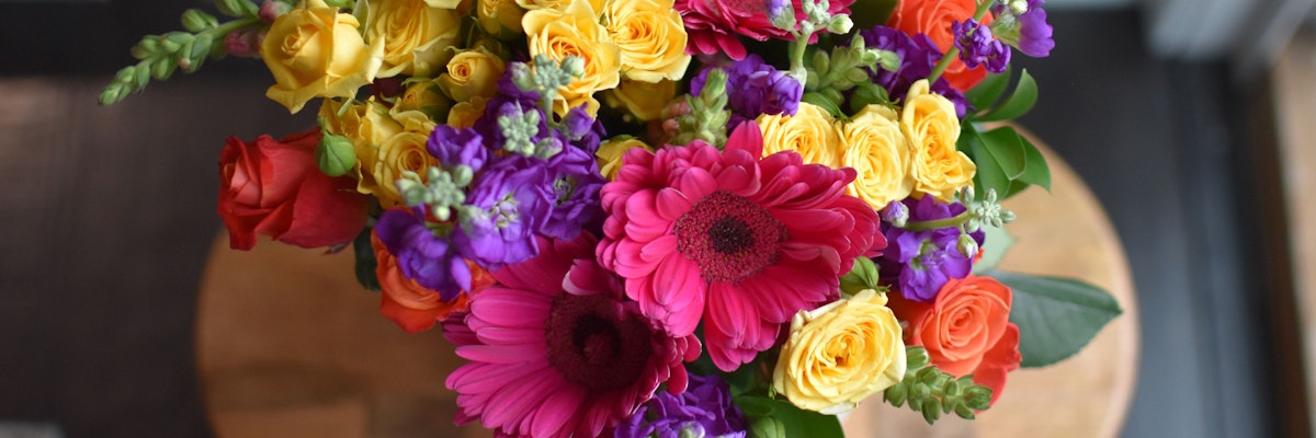 Vibrant floral arrangement featuring roses, gerbera daisies, and assorted colorful blooms.