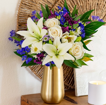Elegant floral arrangement featuring white lilies, roses, and vibrant purple blooms in a vase.