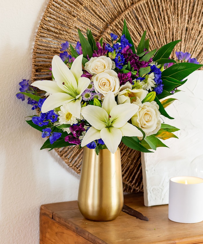 Elegant floral arrangement featuring white lilies, roses, and vibrant purple blooms in a vase.