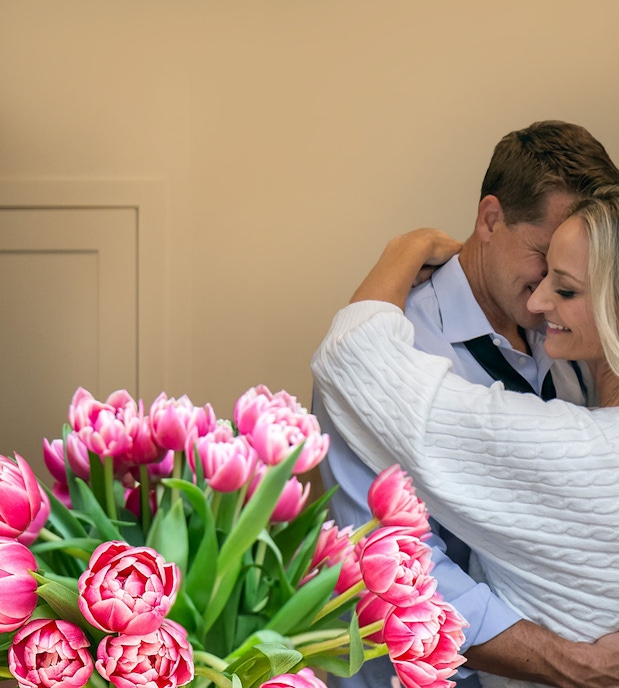 A couple sharing a tender moment, surrounded by a vibrant pink tulip bouquet.