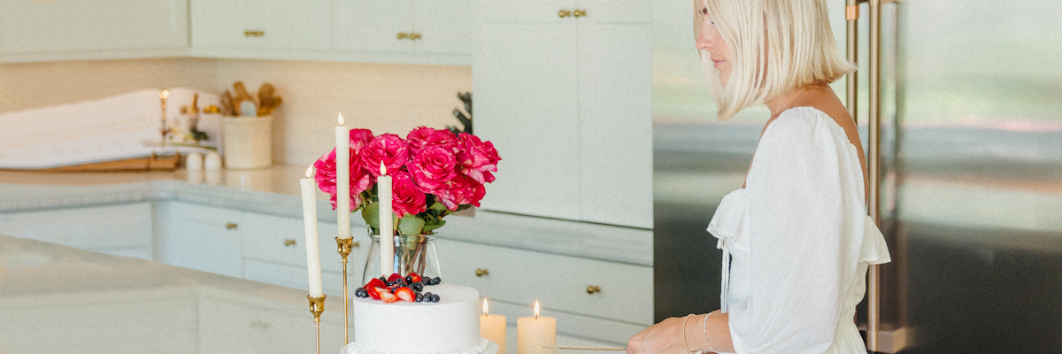 A woman in a white dress elegantly prepares to cut a cake adorned with fresh berries and flowers.