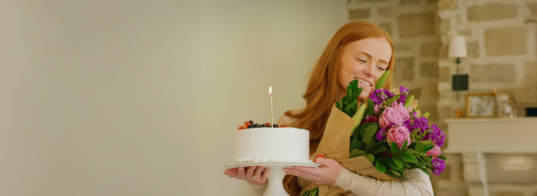 A joyful woman holding a cake and a vibrant bouquet, celebrating a special moment.