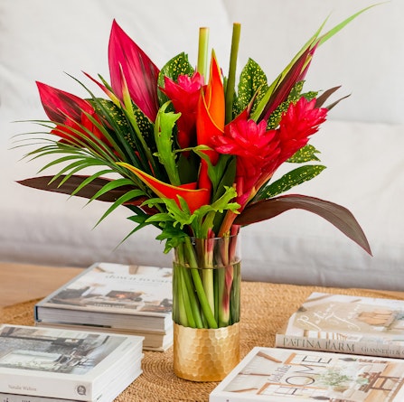 Vibrant tropical flower arrangement featuring red and green foliage in a stylish vase.