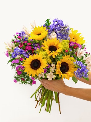 Vibrant bouquet featuring sunflowers, purple flowers, and pink accents, perfect for celebrations.