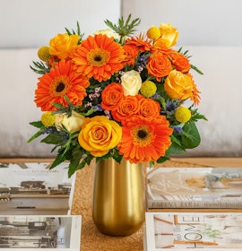 Bright floral arrangement featuring orange gerberas, yellow roses, and greenery in a chic vase.