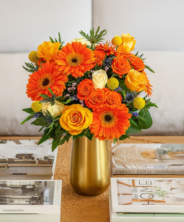 Bright floral arrangement featuring orange gerberas, yellow roses, and greenery in a chic vase.