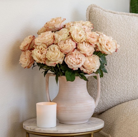 Delicate peach roses beautifully arranged in a soft vase on a stylish side table.