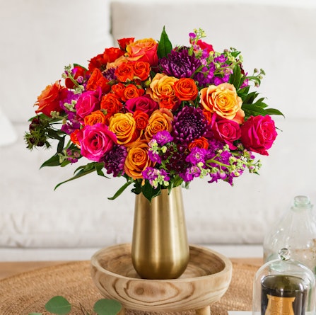 Vibrant floral arrangement featuring roses and purple blooms in a chic gold vase.