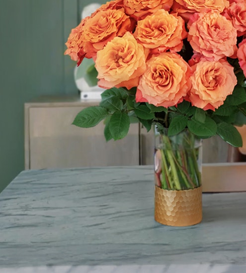 Vibrant orange roses in a stylish gold vase, adding warmth to any decor.