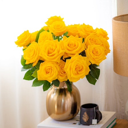 A vibrant bouquet of yellow roses in a golden vase, enhancing a cozy room decor.