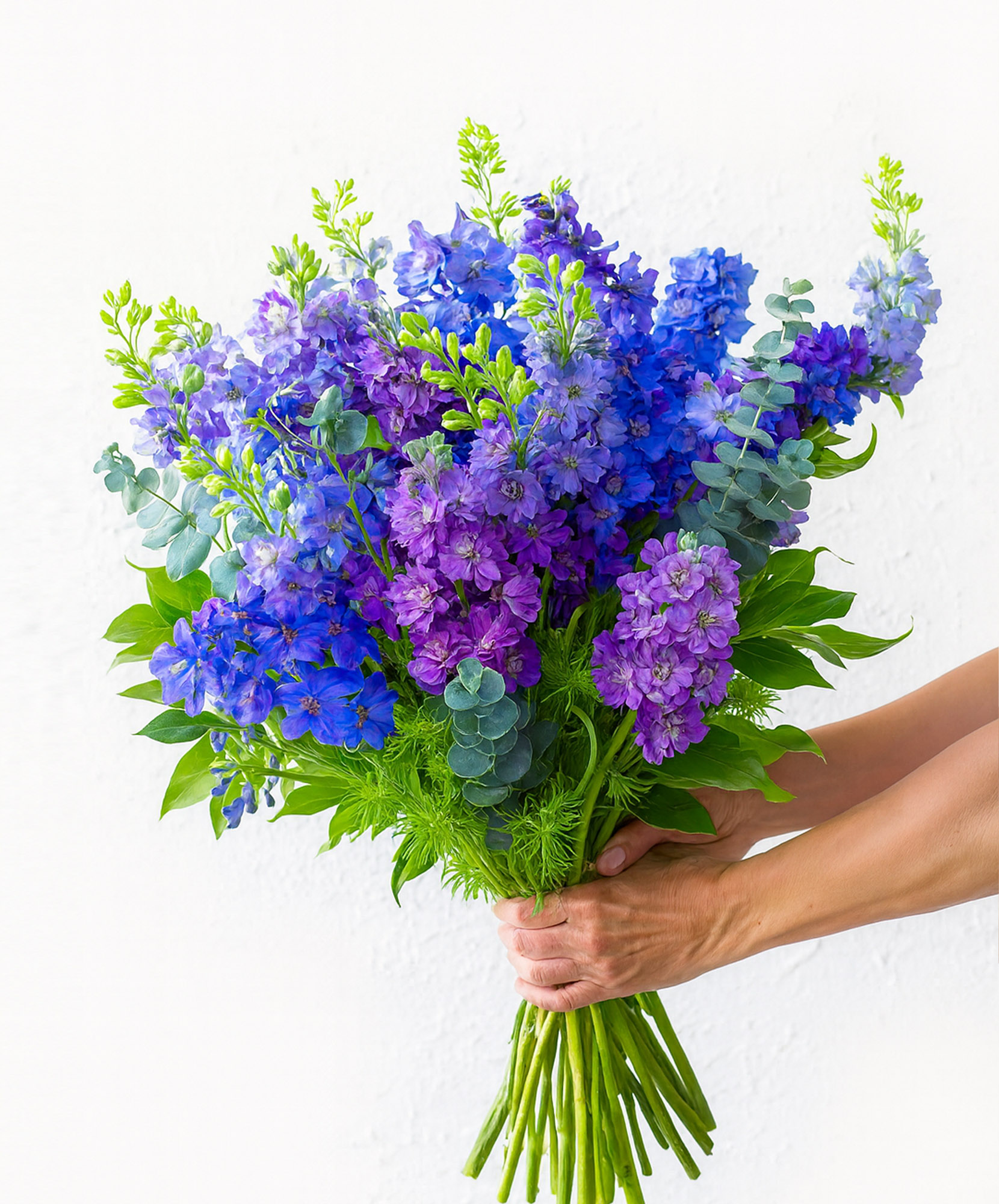 Vibrant bouquet of purple and blue delphiniums with fresh green foliage, ideal for celebrations.