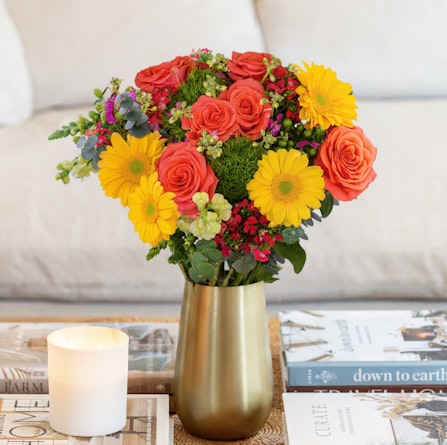 Bright floral bouquet featuring yellow gerbera daisies, orange roses, and lush greenery.