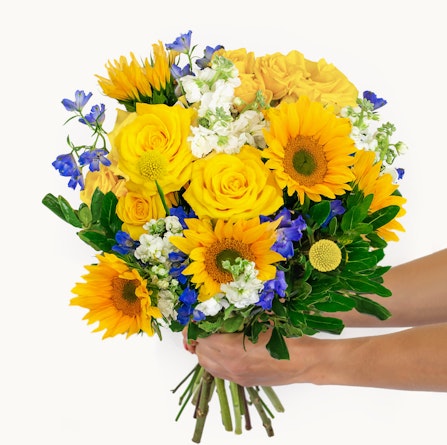 Bright and cheerful bouquet featuring sunflowers, yellow roses, and blue delphinium flowers.
