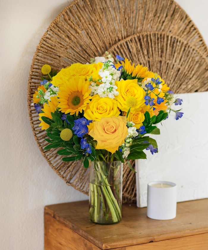 Vibrant yellow sunflower and rose bouquet with blue accents, perfect for brightening any space.