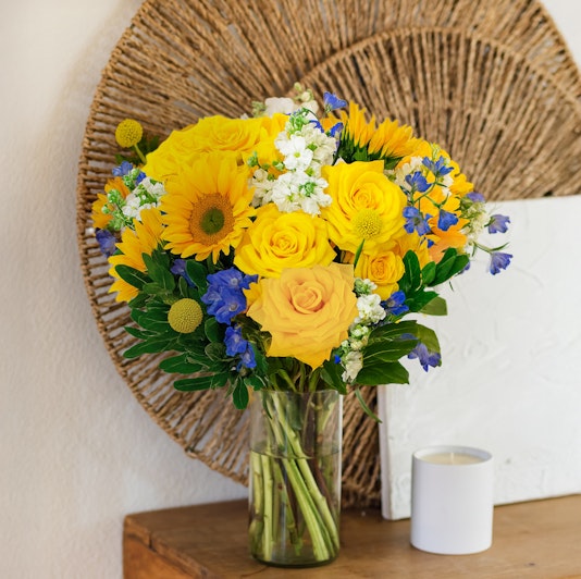 Bright yellow roses and sunflowers in a cheerful vase, perfect for brightening any space.