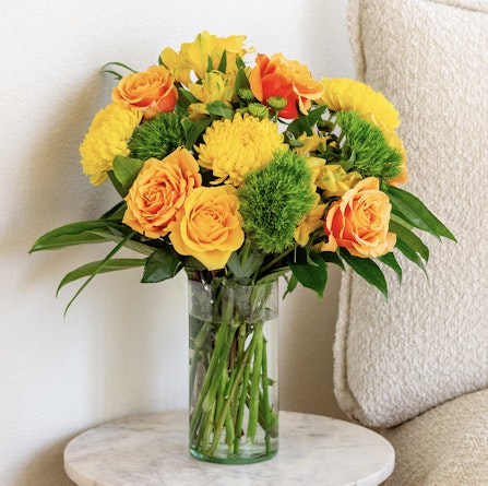 Vibrant bouquet of yellow roses and green flowers in a stylish glass vase, perfect decor.