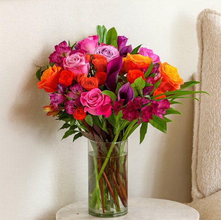 Vibrant mixed floral bouquet featuring roses, calla lilies, and lush greenery in a vase.
