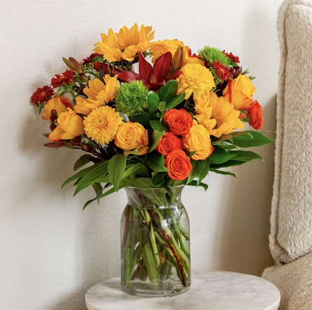 Bright floral arrangement featuring sunflowers, orange roses, and vibrant seasonal blooms.