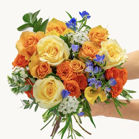 Vibrant bouquet of orange and yellow roses, accented with blue flowers and greenery.