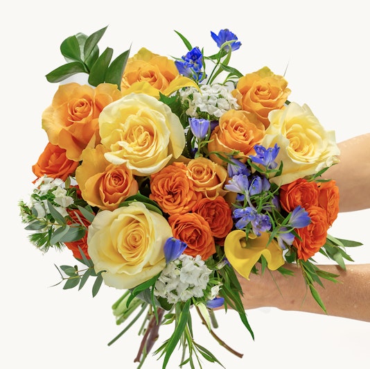 Vibrant bouquet of orange and yellow roses, accented with blue flowers and greenery.