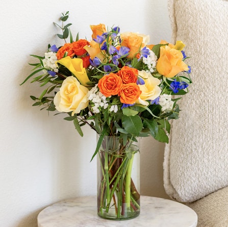 Vibrant bouquet of orange and yellow roses with blue accents, perfect for brightening up any space.