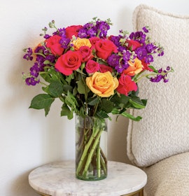 Bright and colorful bouquet featuring red, orange, and purple flowers in a glass vase.