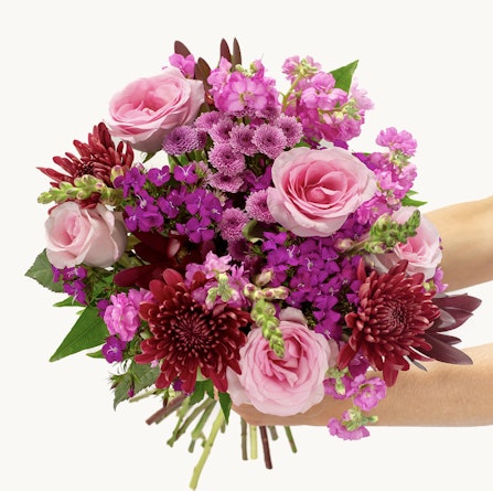 Vibrant bouquet featuring pink roses, purple flowers, and deep red chrysanthemums, beautifully arranged.