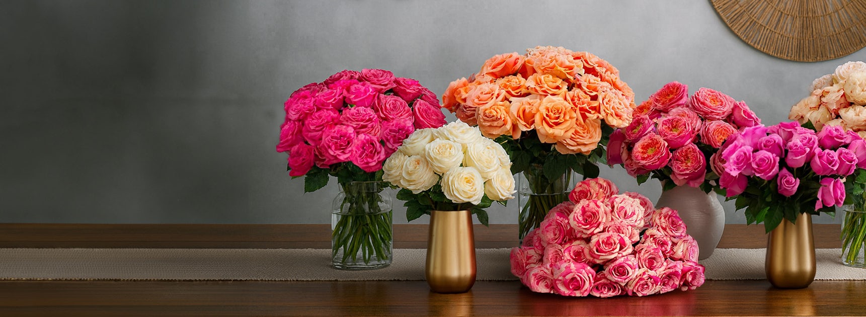 Vibrant floral display featuring pink, orange, and white roses in elegant vases on a table.