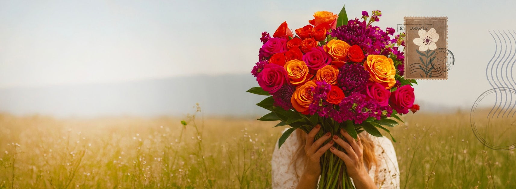 Vibrant bouquet of roses and wildflowers held by a woman in a sunny field, perfect for celebrations.
