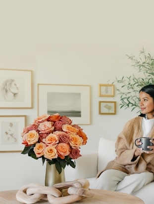 Elegant woman enjoying a warm drink beside a vibrant rose bouquet in an artistic setting.