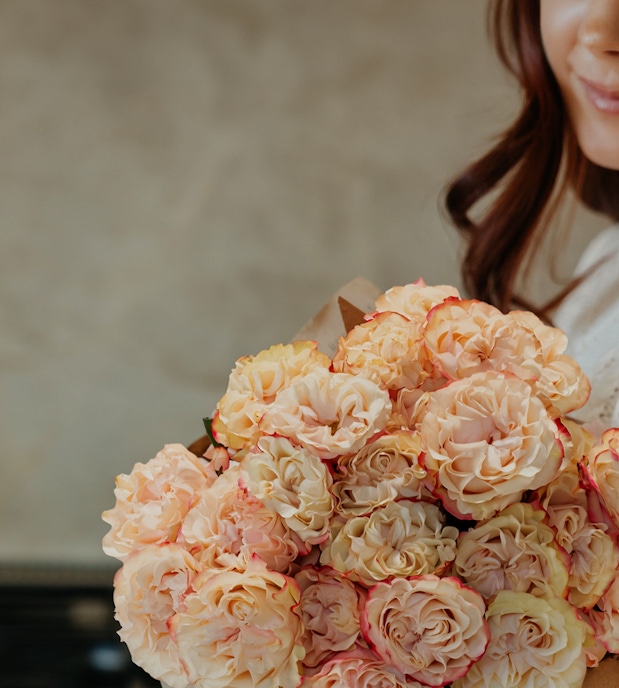 A beautiful bouquet of soft peach and cream roses held by a woman, radiating elegance.