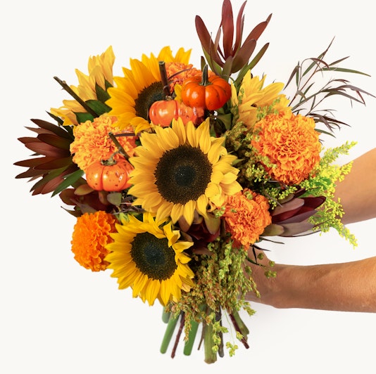 Vibrant floral bouquet featuring sunflowers, marigolds, and miniature pumpkins in autumn hues.
