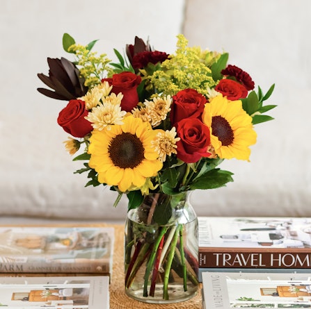 Vibrant bouquet featuring sunflowers, red roses, and assorted daisies in a chic vase.