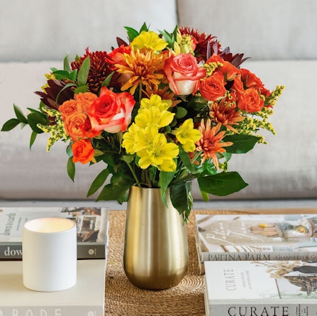 Vibrant floral arrangement of red and yellow flowers in a chic gold vase on a coffee table.