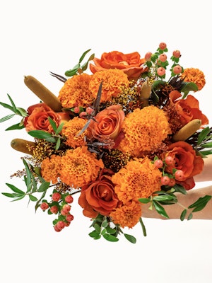 Vibrant bouquet of orange roses and marigolds, accented with lush greenery and berries.