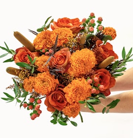 Vibrant bouquet of orange roses and marigolds, accented with lush greenery and berries.