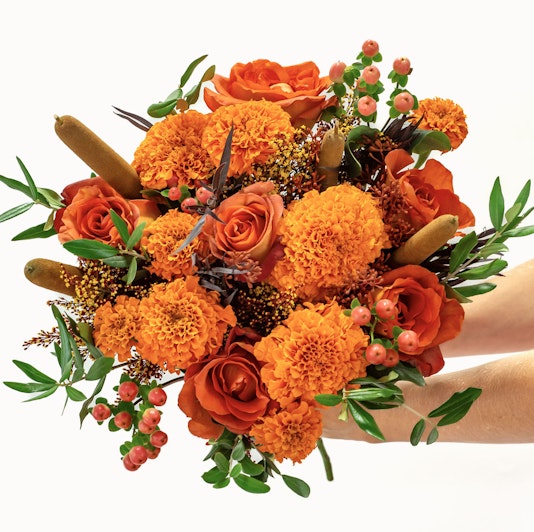 Vibrant bouquet of orange roses and marigolds, accented with lush greenery and berries.