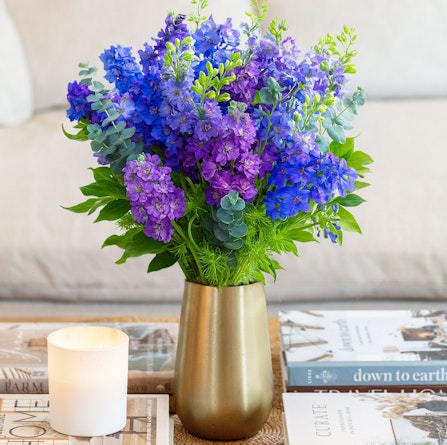 Vibrant purple floral arrangement featuring delphiniums and greenery in a stylish vase.